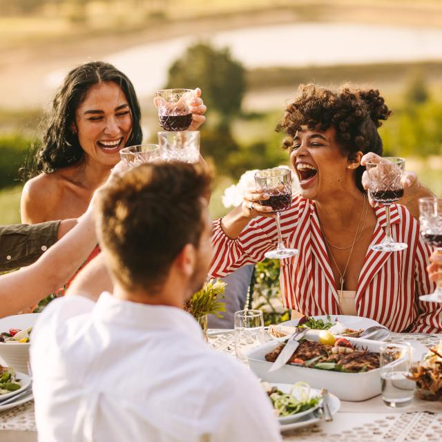 Gruppe fröhlicher Freunde, die bei einer Dinnerparty Wein trinken. Multiethnische Menschen, die draußen zusammenkommen.