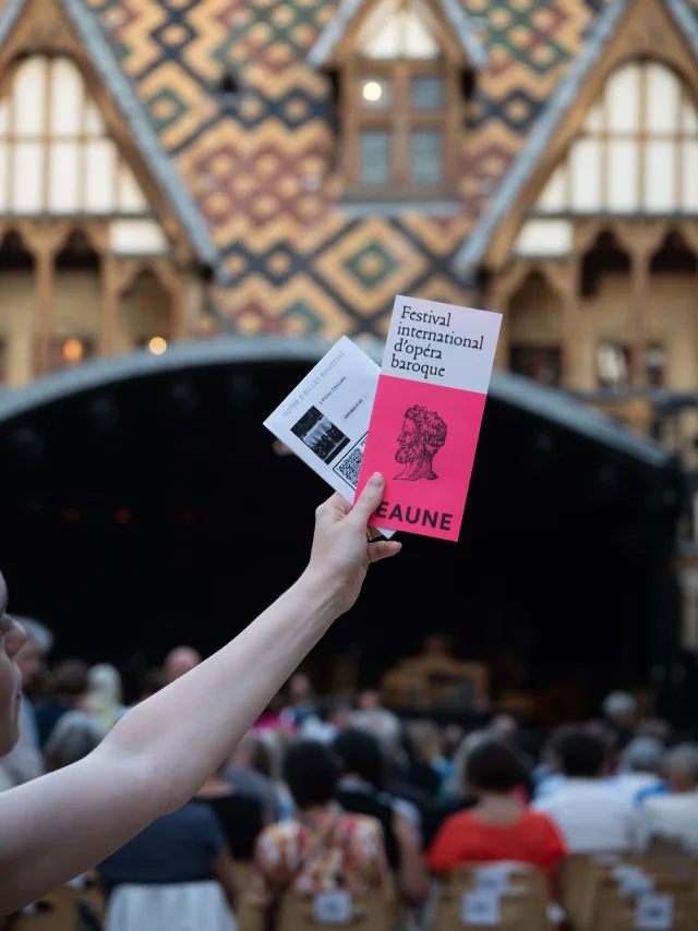 main tendant un flyer dans la cour des Hospices de Beaune